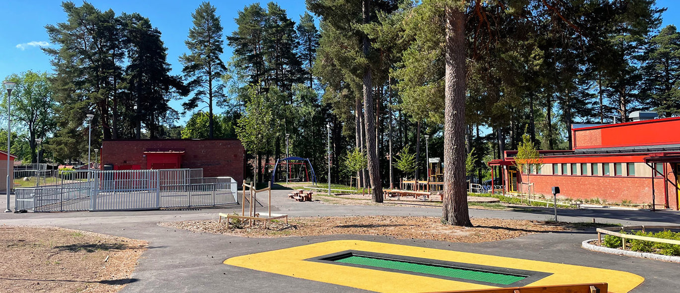 Legeplads med parkbænke, nedgravet trampolin og multibane i baggrunden